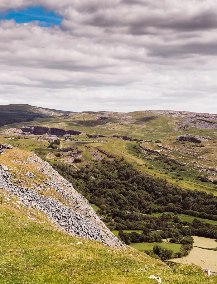 dwy fenyw’n cerdded ar fryn gyda golygfeydd gwledig.