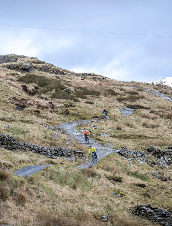 Dau feiciwr mynydd yn reidio i lawr llwybr troellog yn Antur Stiniog.