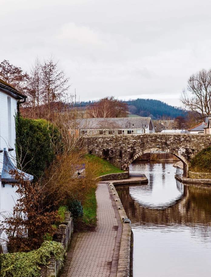 Pont garreg fechan dros yr afon a thai i'r ochr ac yn y pellter