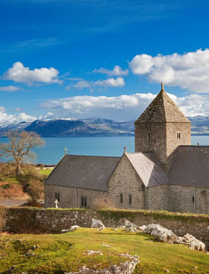 Hen adeilad carreg gyda'r môr a mynyddoedd yn y cefndir
