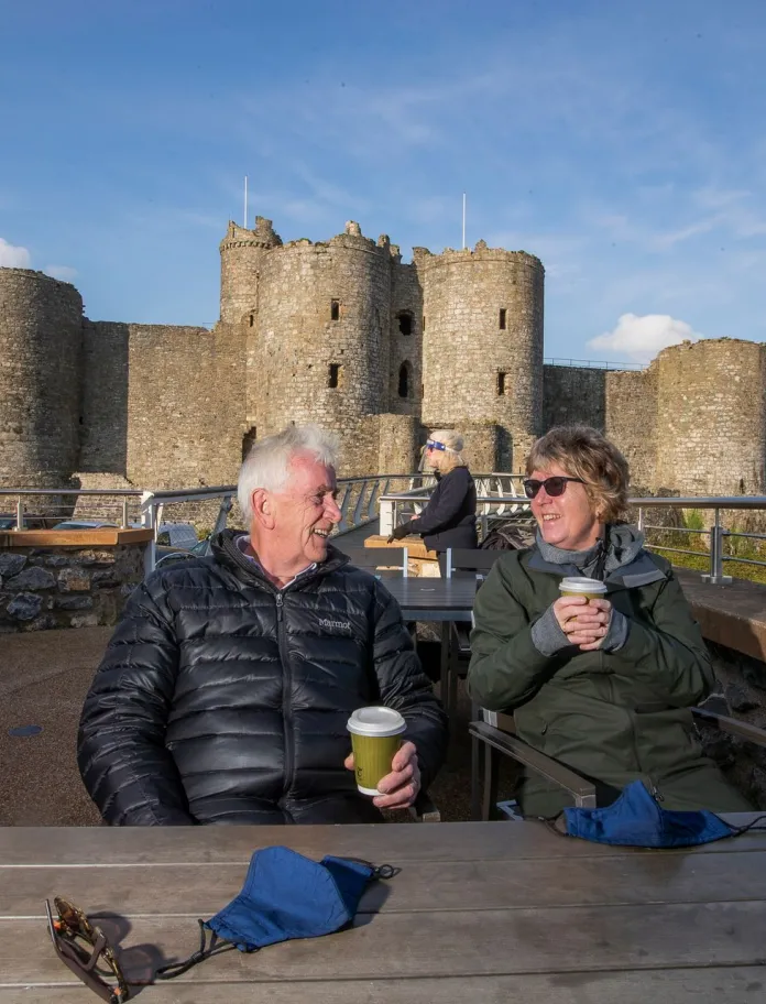 Cwpwl yn mwynhau coffi ger castell hanesyddol