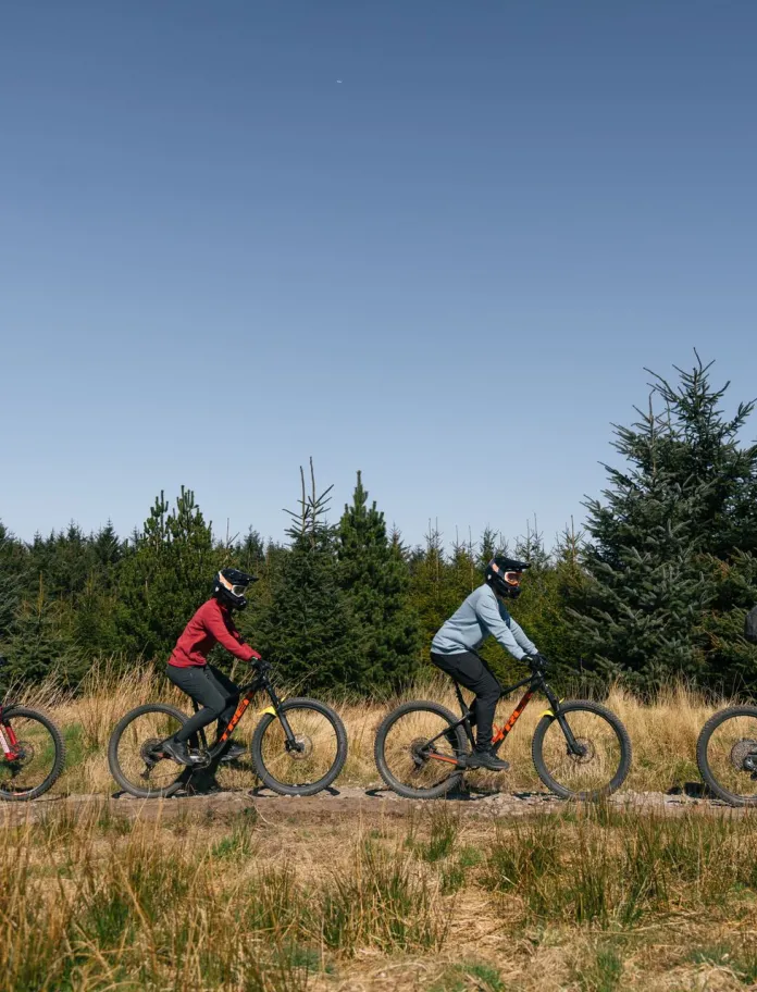 pedwar person mewn llinell ar gefn beic mynydd ar llwybr yn bikepark Cymru.