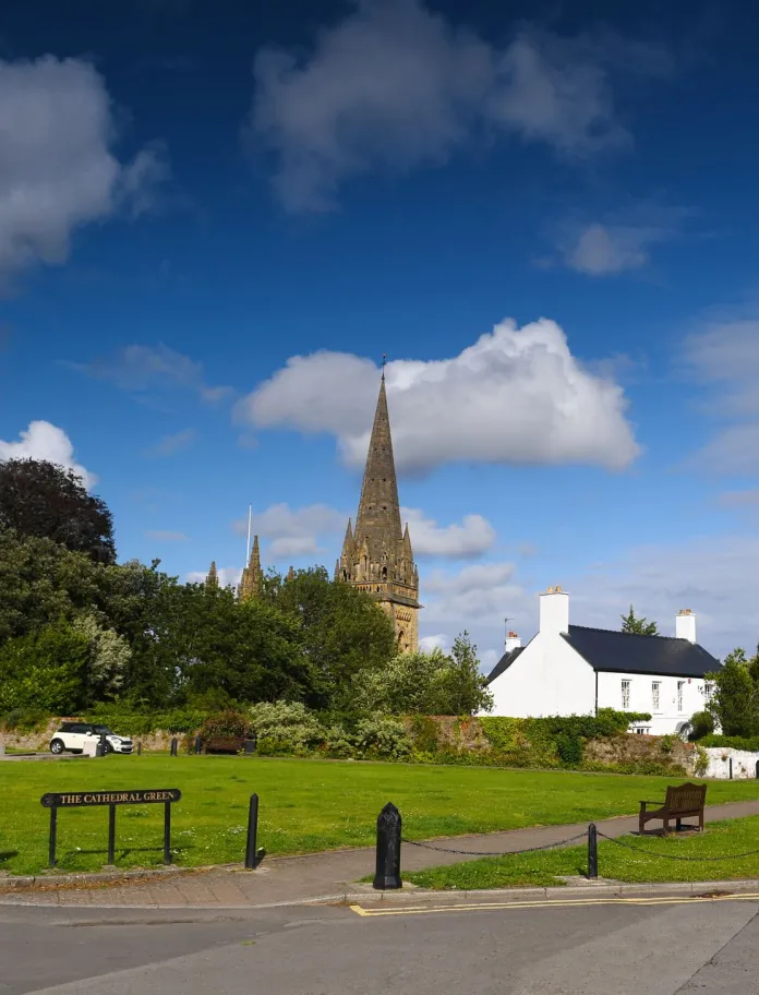 Eglwys Gadeiriol Llandaf a Cathedral Green gyda lawnt agored, meinciau a beicwyr yn pasio ar y ffordd yng Nghaerdydd