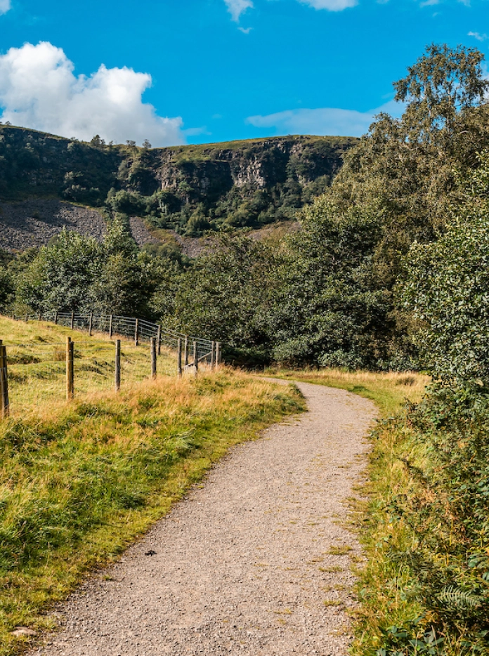 Llwybr cerdded o gwmpas cae gyda tharren werdd y tu cefn.