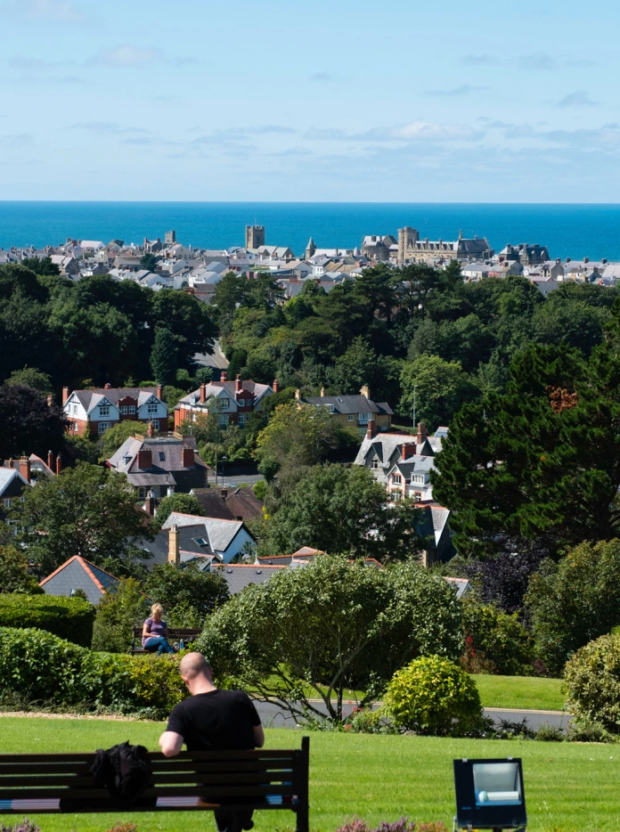 Dyn yn eistedd ar fainc, yn edrych i lawr dros Aberystwyth