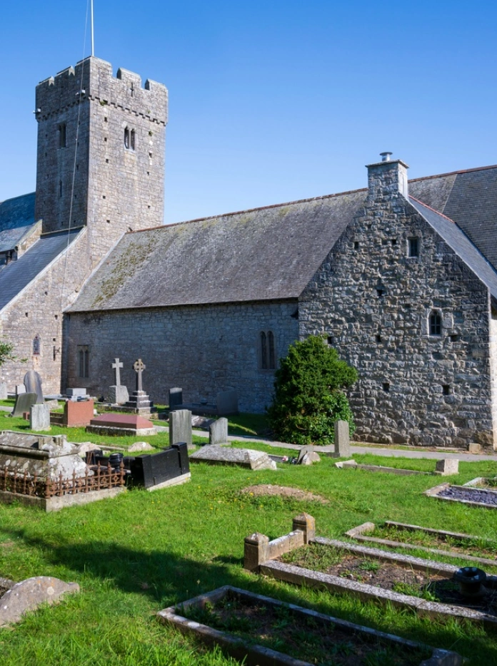 Golygfa allanol o Eglwys Sant Illtyd gydag awyr las a beddau y tu allan
