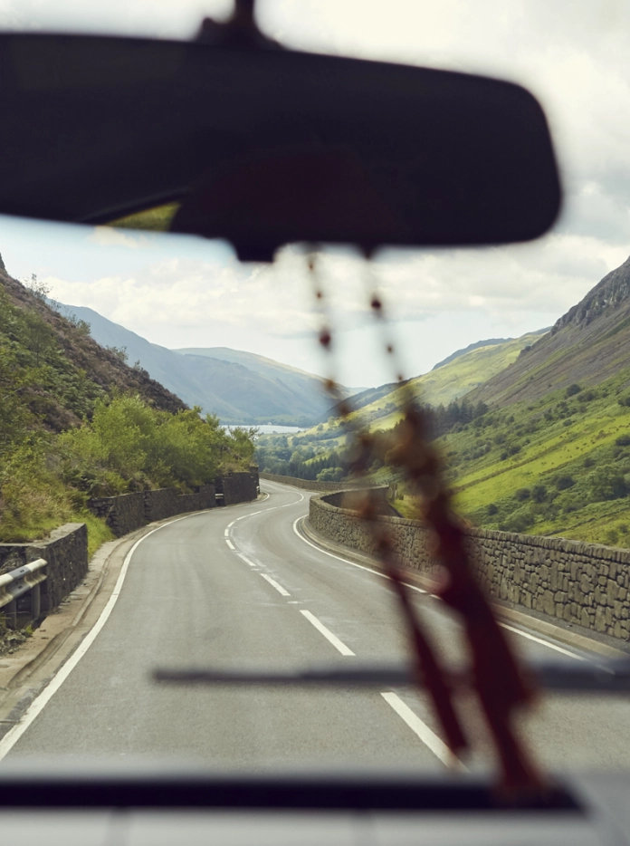 Golygfa trwy ffenestr car gyda mynyddoedd a llyn ar y gorwel.