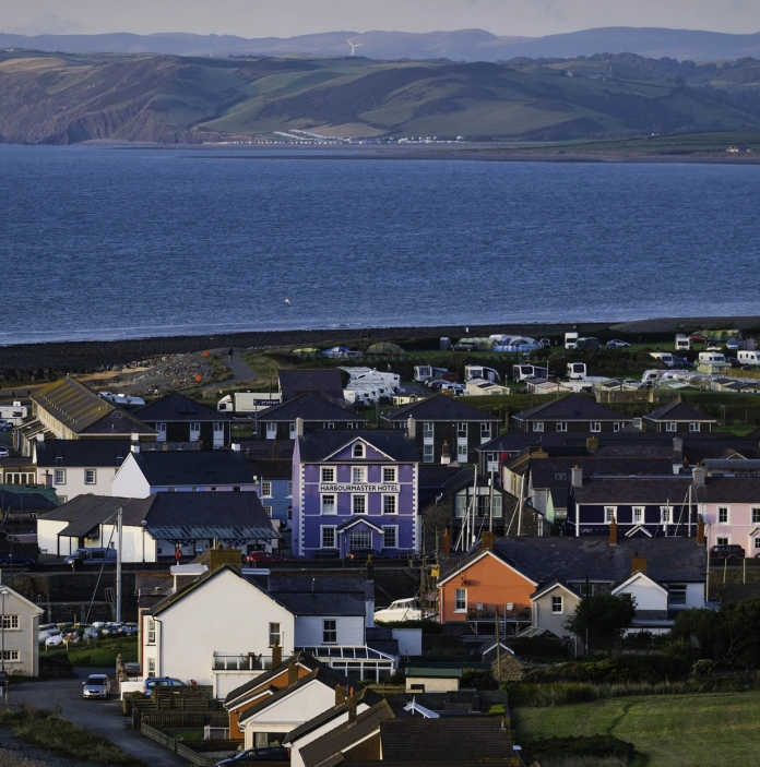 Golygfa o arfordir Aberaeron gyda tai a mynyddoedd