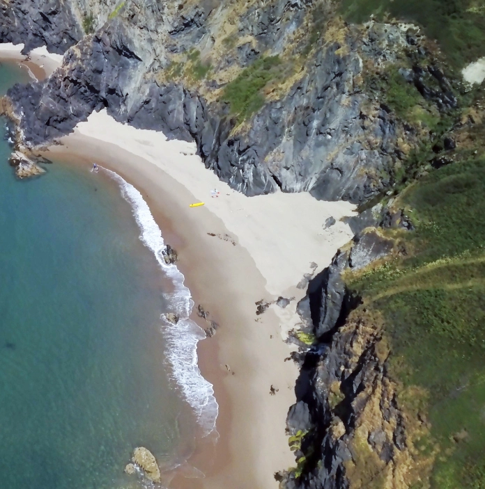 Llun o'r awyr o draeth Llangrannog a'r creigiau