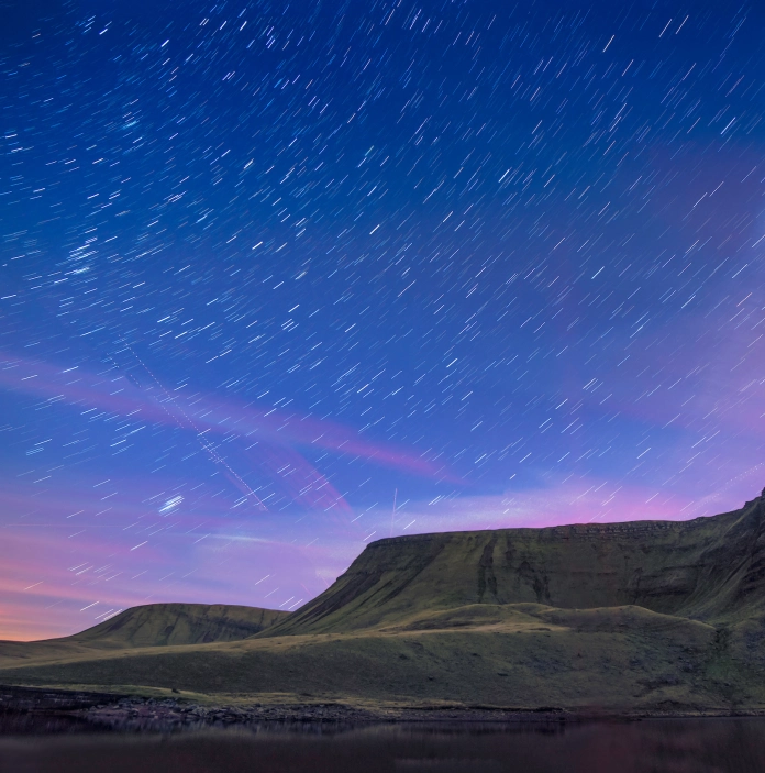 Llun o olion y sêr yn yr awyr, uwchben y llyn gyda mynyddoedd yn y cefndir