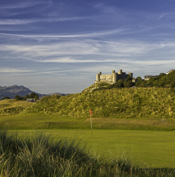 Golygfa o gwrs golff a'r grîn gyda'r goes fflag, a Chastell Harlech ar fryn yn y cefndir
