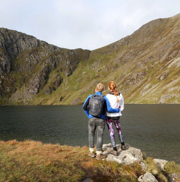 Llun o ddau gerddwr wrth Lyn Cau yn edrych tuag at Graig Cau (canol) a Phenygadair (dde)
