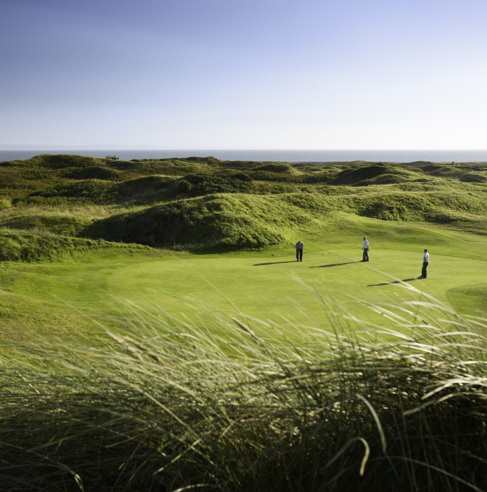 Three men playing golf on the green with the sea in the distance