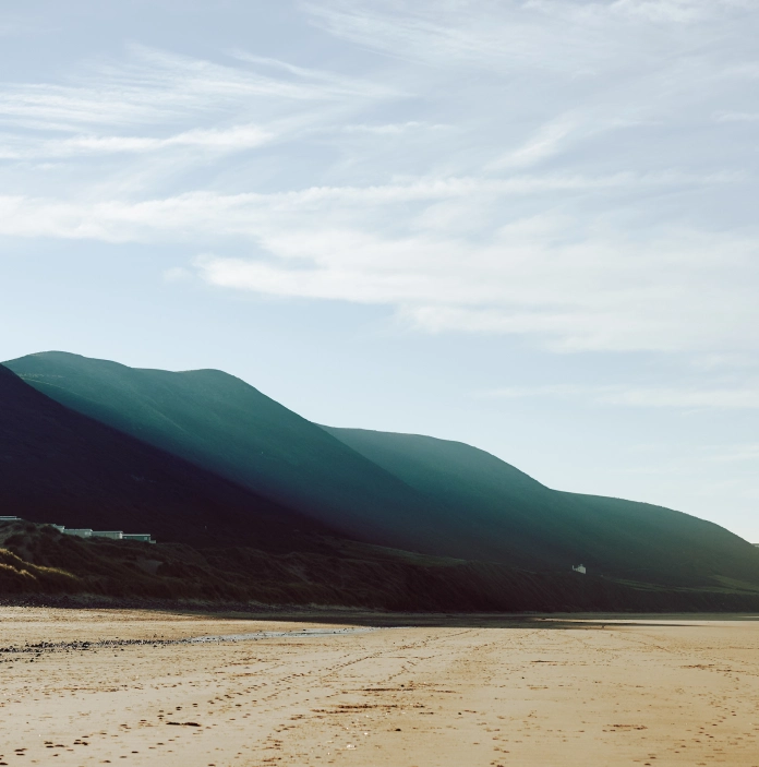 Traeth tywodlyd gyda bryniau yn y cefndir