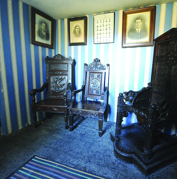 Ystafell gyda thair cadair eisteddfodol fawr a lluniau teuluol ar y wal