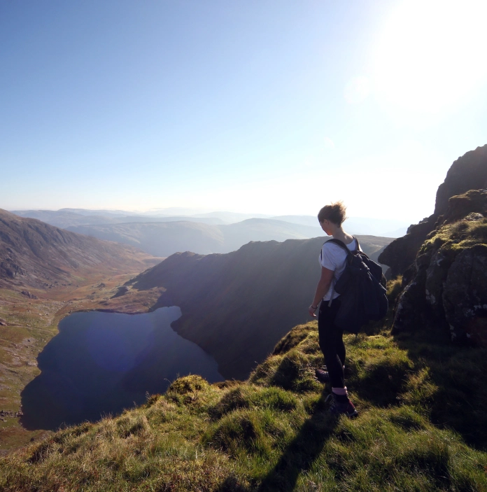 Cerddwr yn sefyll ar fynydd ac yn edrych lawr ar y llyn