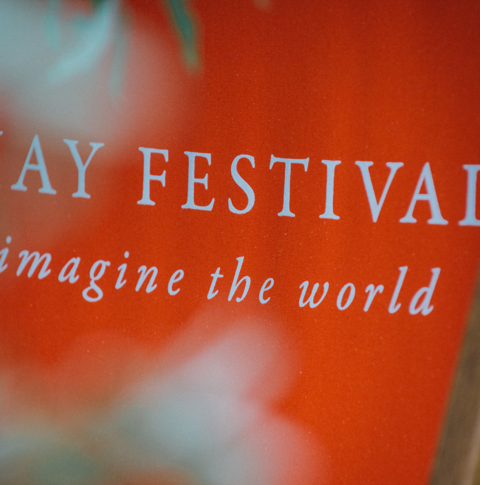 Cadair haul goch yn dweud 'HAY FESTIVAL imagine the world' mewn ysgrifen gwyn.