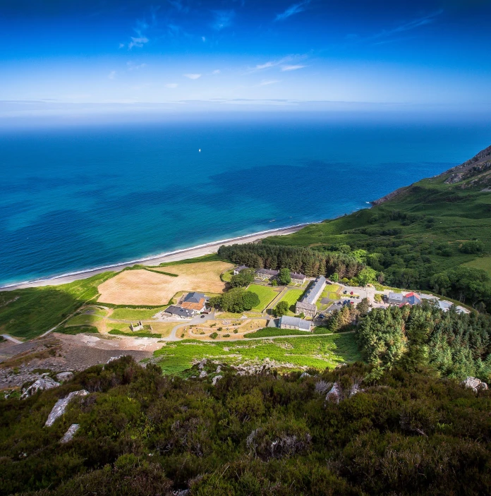 Llun o'r awyr yn edrych i lawr ar y pentref, gyda choed ar un ochr a'r môr ar yr ochr arall