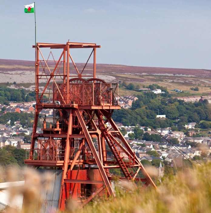 Olwyn pwll glo coch gyda golygfa o'r dyffryn yn y cefndir