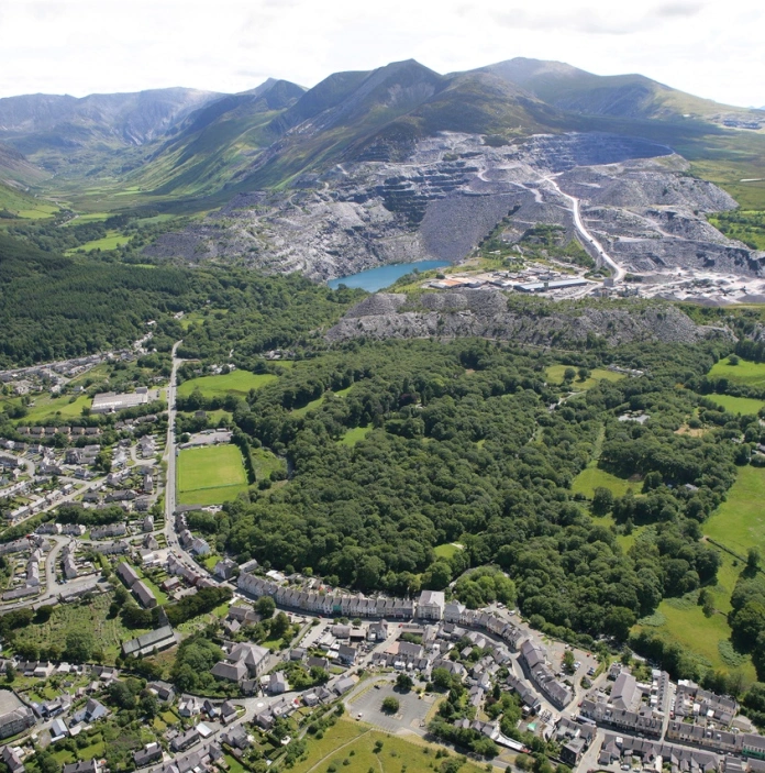 Llun o'r awyr o ardal chwareddyol Bethesda a Phenrhyn. Mae nifer o gaeau a choed gwyrdd rhwng ardal boblog o dai a thirwedd fynyddig y chwareli.
