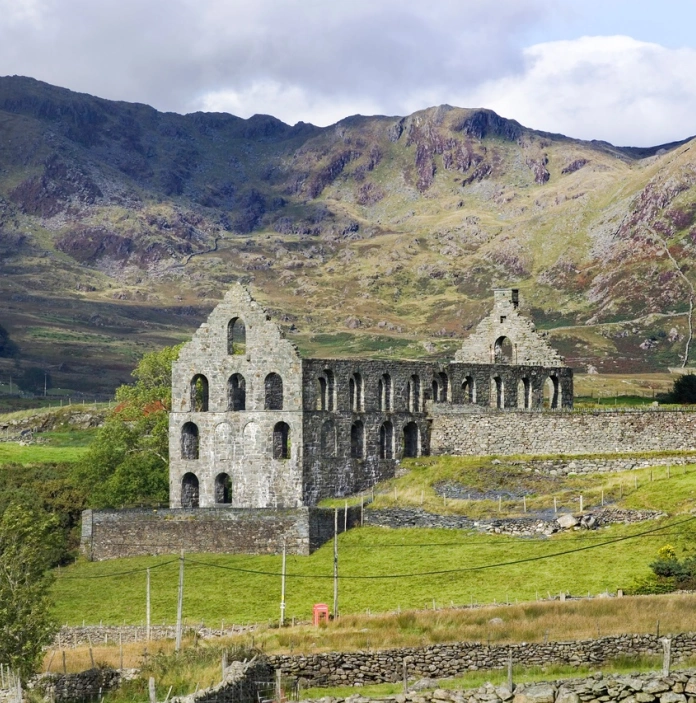 Adfeilion hen felin chwarel mewn dyffryn gyda mynyddoedd o'i gwmpas.