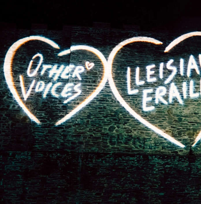 Dwy galon wedi taflunio ar gastell gyda'r geiriau Other Voices / Lleisiau Eraill.