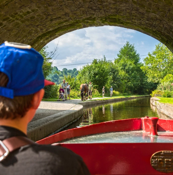 Bachgen ar cwch coch yn teithio ar gamlas Llangollen
