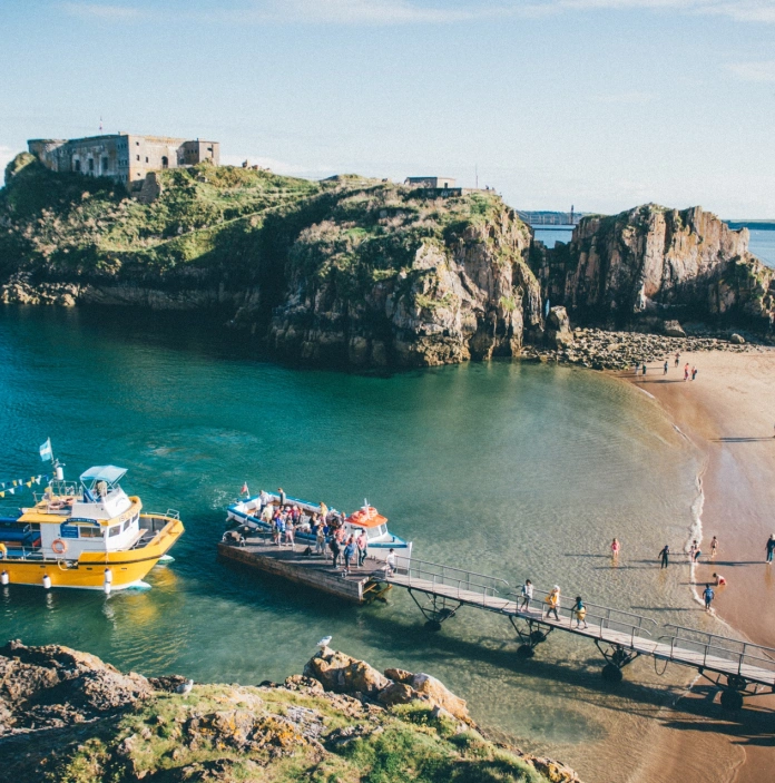 Llun o Gaer Ynys Catrin ar Ynys Catrin, a chychod bach yn casglu teithwyr o Ddinbych-y-pysgod