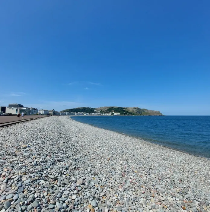 Promenâd a thraeth cerrig mân ar ddiwrnod heulog.
