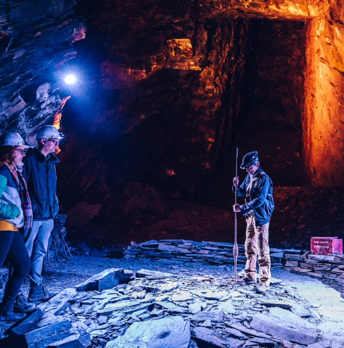 A man showing slate mine tools to a tour group in an underground cavern.