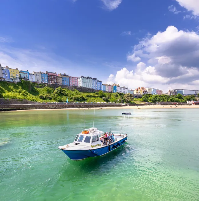 A small fishing boat in gorgeous blue seas, with a colourful harbour village in the background.