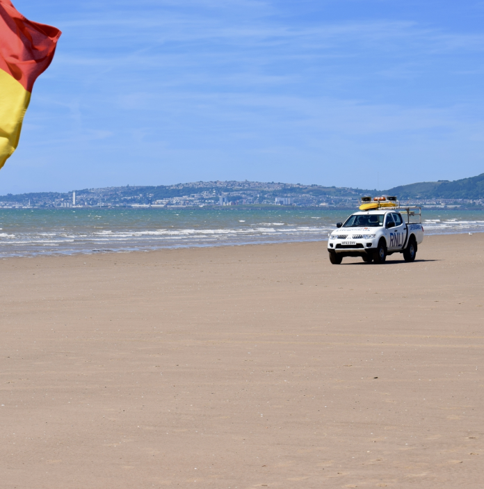 Achubwyr bywyd yn patrolio'r traeth mewn cerbyd