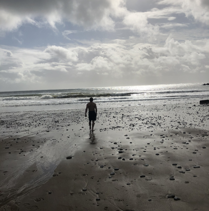 Llun o ddyn yn cerdded ar y traeth tuag at y môr ym Mae Pwll Du
