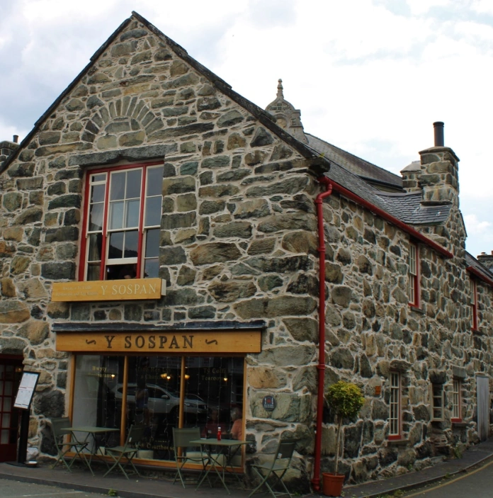 Hen adeilad cerrig gyda ffenestri a drws coch ac arwydd melyn yn dweud Y Sospan.