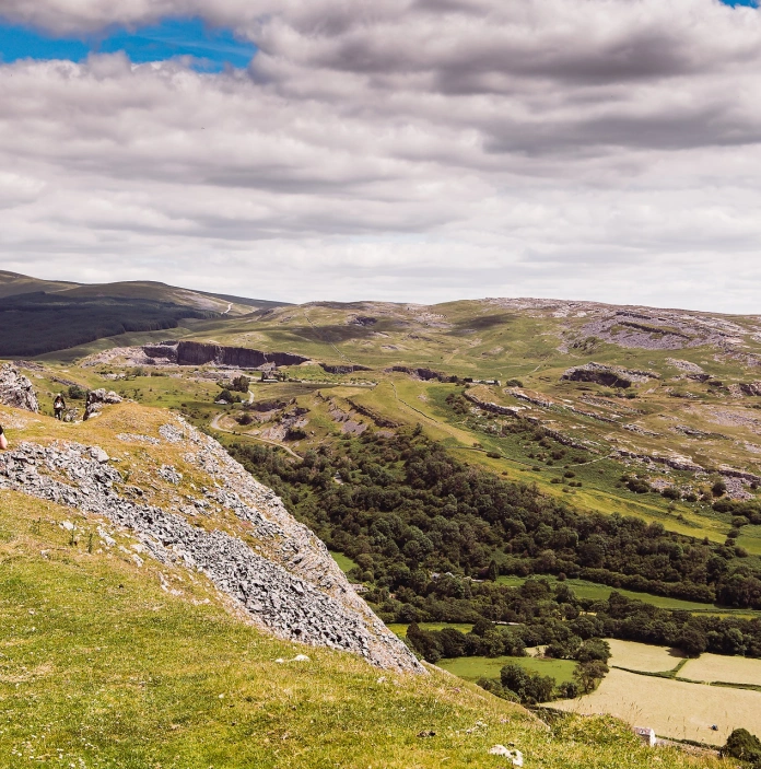 dwy fenyw’n cerdded ar fryn gyda golygfeydd gwledig.