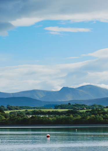 Llun o'r môr gyda choed a bryniau yn y pellter.