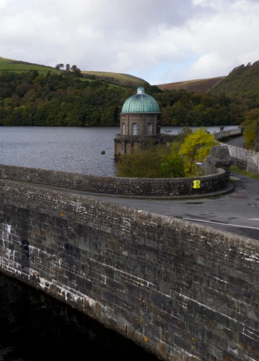 llun o'r afon yn cael ei dal yn ôl gan yr argae gyda choedwig a mynyddoedd yn y cefndir