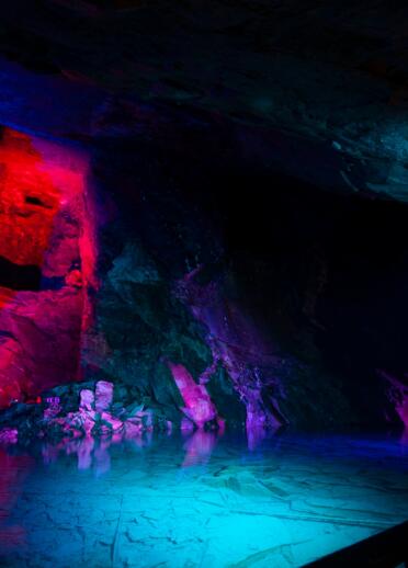 Slate cavern and natural spring water lit up with brightly coloured lights.