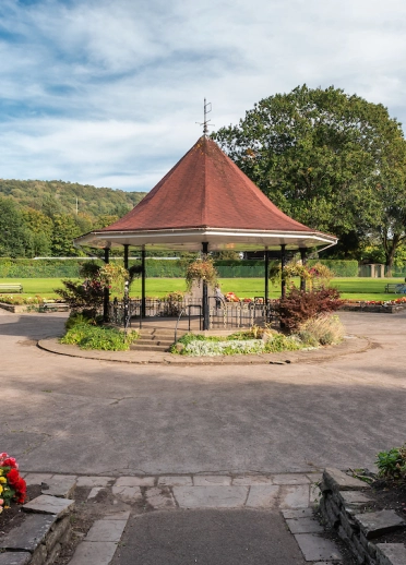 Bandstand yng nghanol parc gyda blodau lliwgar o'i amgylch ac awyr laws yn gefndir.