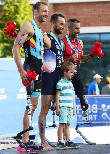 Tri dyn a bachgen bach â medalau ar bodiwm.