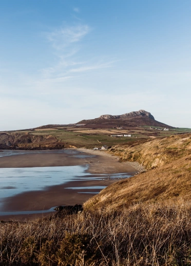 Golygfa o draeth ar ôl i'r llanw fynd allan gyda mynyddoedd yn y cefndir