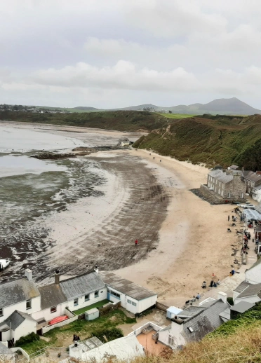 Llun yn edrych i lawr ar draeth Porthdinllaen gyda thai yn y tu blaen a'r bryniau yn y cefndir