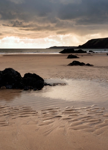 Llun o'r traeth wrth iddi fachlud a'r môr yn y pellter