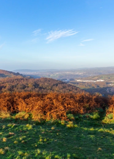golygfeydd o gopa mynydd, yn edrych dros dref, gyda bryniau gwyrdd o’i hamgylch.