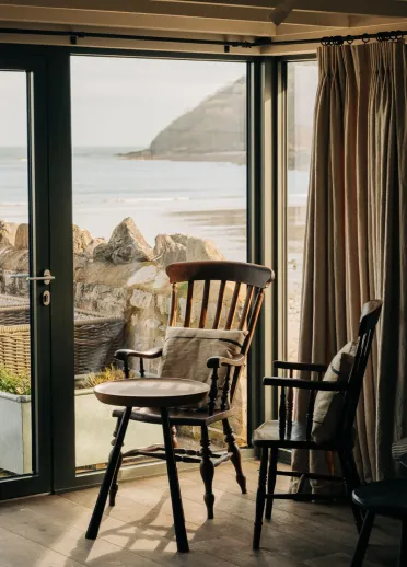 Golygfa drwy ddrysau patio agored tuag at yr arfordir, gyda llefydd i eistedd mewn bwyty y tu mewn.