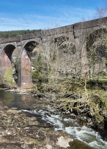dŵr yn llifo a thraphont Pontrhydyfen yn y cefndir.