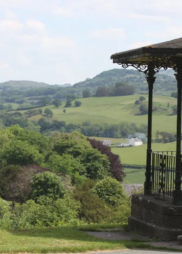 bandstand a pharc gyda choed a bryniau yn y cefndir.