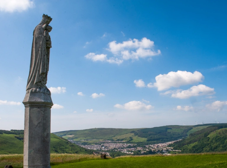 Cerflun o Sant gyda llethrau tonnog a thref y tu ôl