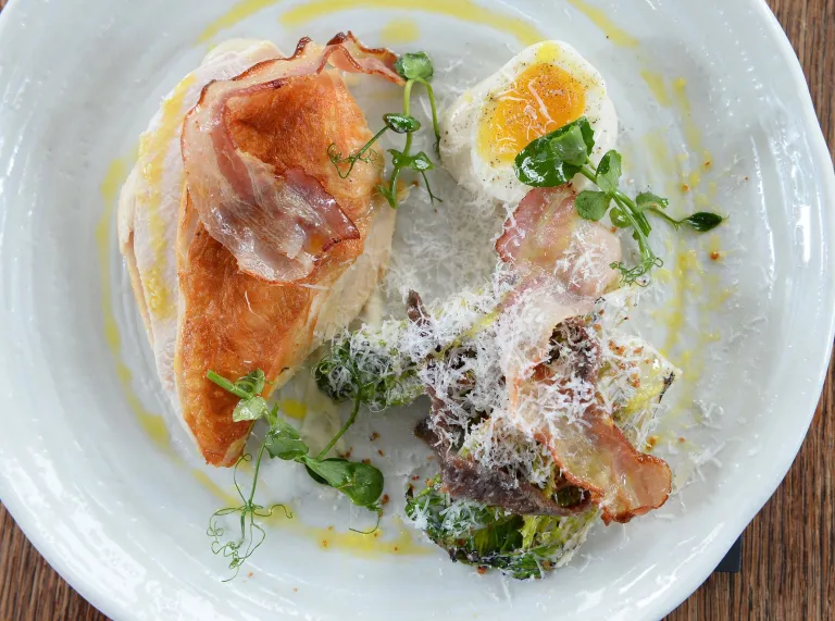 Brest cyw iâr, bacwn, caws parmesan a deiliach ar blât.