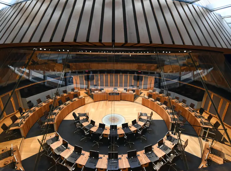 Cadeiriau a byrddau wedi’u gosod mewn cylch yn siambr ddadlau adeilad y senedd.